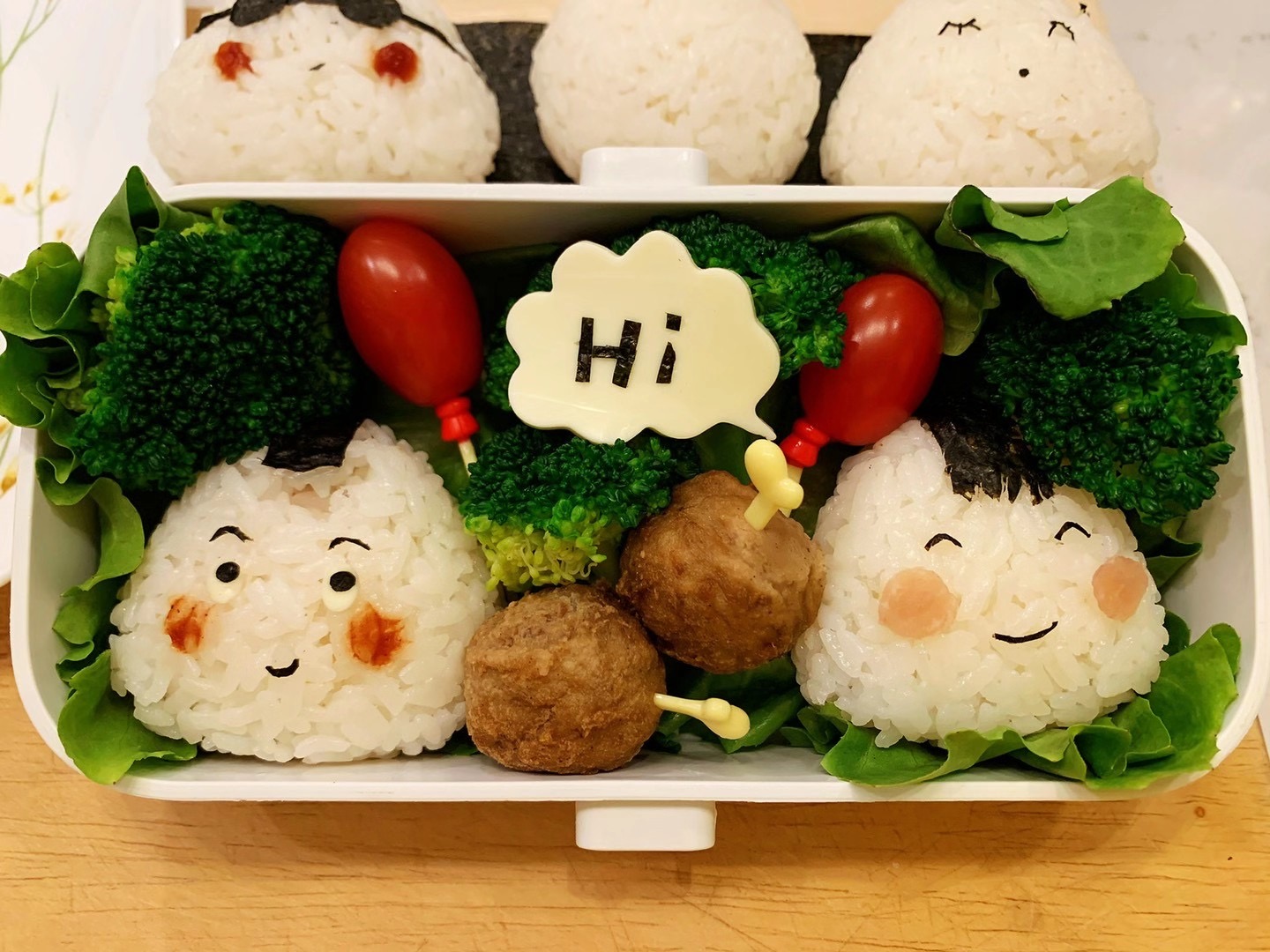 Bento box meal with emoji-faced rice balls