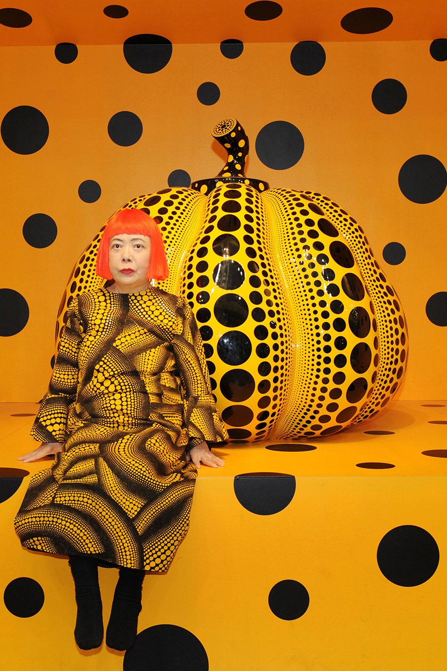 Yayoi Kusama sitting in front of a giant glass pumpkin