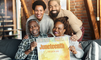 Smiling African American family of 4 holding a sign that says Juneteenth Freedom Day