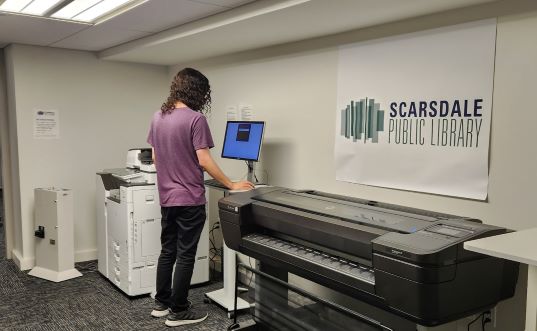 A person releasing a print job, standing next to a copier.