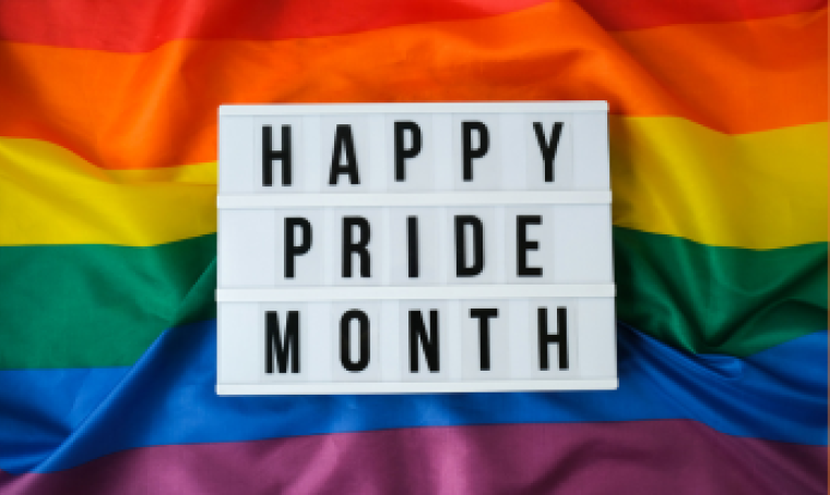 Happy Pride month written on a white rectangle on top of a rainbow pride flag