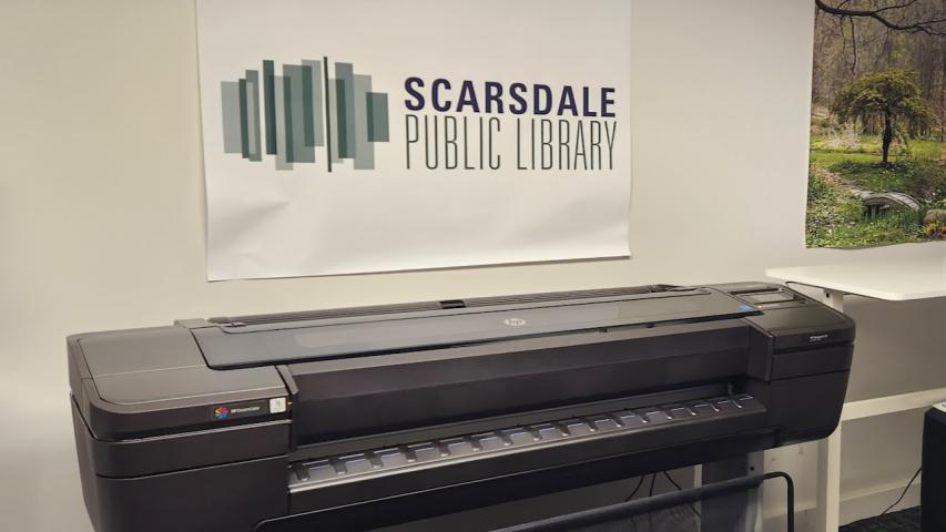 The poster printer against the wall under a Scarsdale Library poster